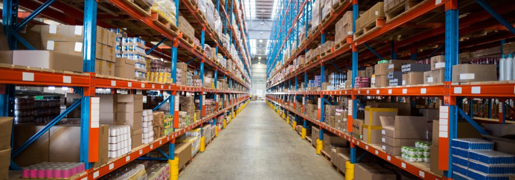 Corredor de armazém com prateleiras altas organizadas e produtos distribuídos por categorias, ilustrando o processo de mapeamento de estoque.